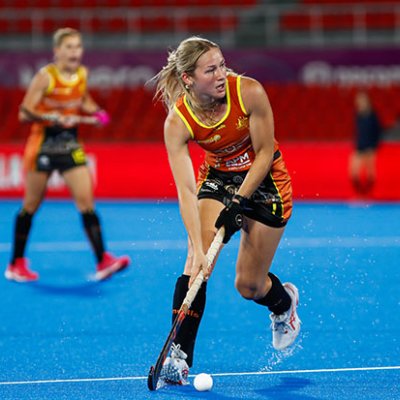 A young hockey player guiding the ball with her stick on a blue hockey field